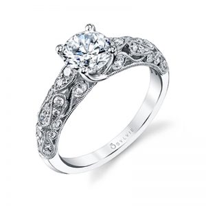 A white gold diamond engagement ring from the Sylvie Collection featuring diamond accented swirling shapes and a large center diamond with prongs that cross over each other
