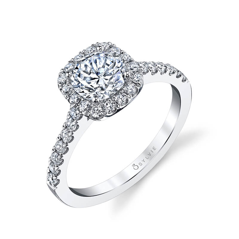 A white gold diamond engagement ring from the Sylvie Collection features a round diamond in the center with a cushion shaped halo around it
