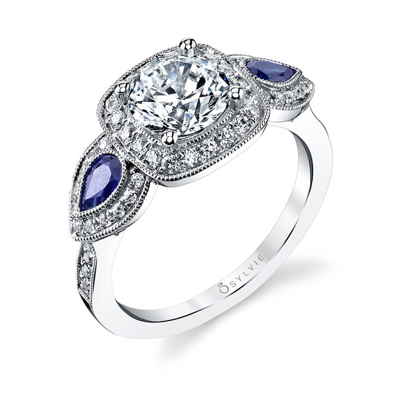 A white gold diamond three-stone halo engagement ring from the Sylvie Collection with large pear shaped sapphires on either side of the center stone